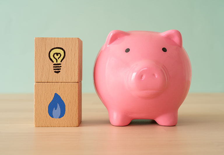 A pink piggy bank on a table next to two stacked wooden blocks with gas and electricity symbols on them
